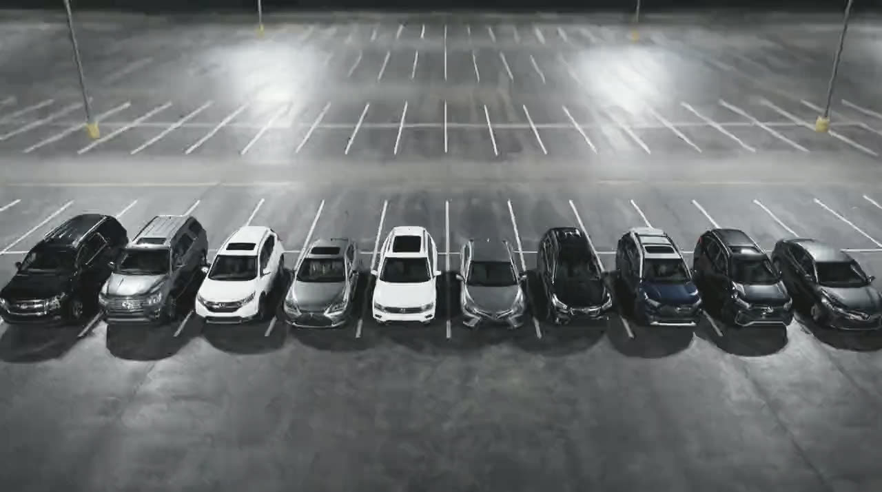 The same ten vehicles seen from above and to one side, parked in marked bays on an empty lot at night.